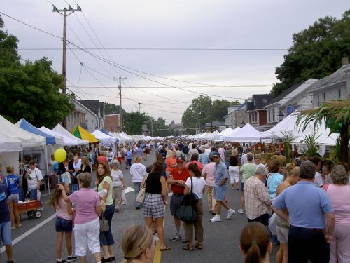 A bustling street fair with numerous tents, vendors, and a large crowd of people enjoying the event.