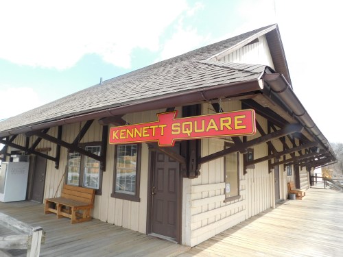 Exterior of a building with a sign reading "KENNETT SQUARE," featuring wooden architecture and a deck.
