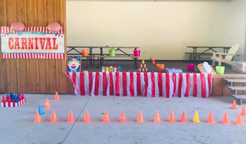 A carnival booth with red and white stripes, colorful cones, and games set up in a spacious area.