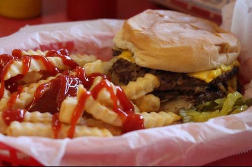 A cheeseburger with lettuce in a bun, served with crinkle-cut fries drizzled with ketchup.