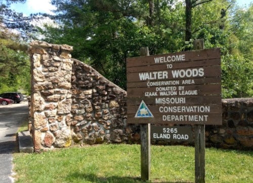 Sign welcoming visitors to Walter Woods Conservation Area, with stone entrance and greenery in the background.