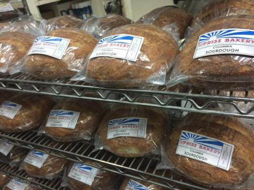 Loaves of sourdough bread packaged in clear bags, displayed on a wire rack in a bakery.