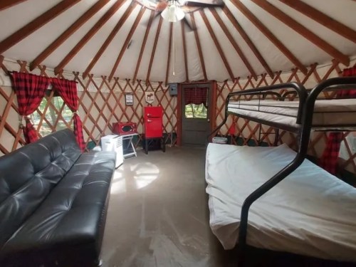 Interior of a yurt featuring a black sofa, bunk beds, and rustic decor with plaid curtains.