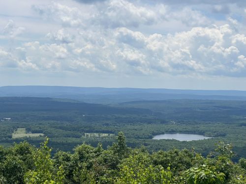 A panoramic view of lush green hills and a serene lake under a partly cloudy sky.