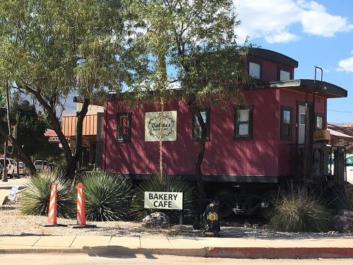 A pink train caboose converted into a bakery café, surrounded by desert plants and blue skies.