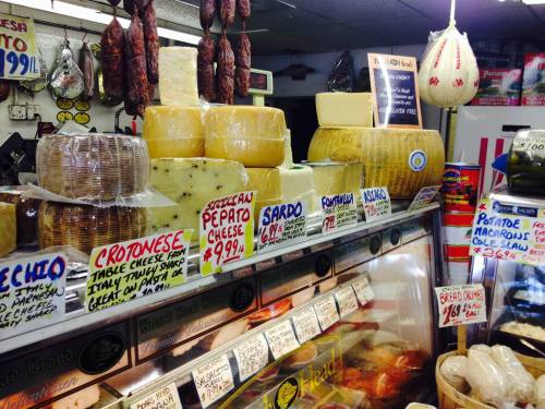 A display of various cheeses and cured meats in a deli, with price tags and signs indicating different products.