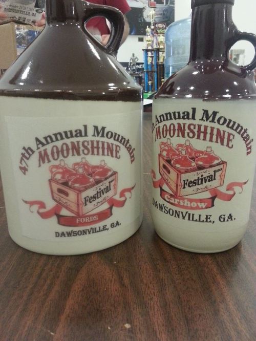 Two decorative jugs labeled for the 47th Annual Mountain Moonshine Festival and Car Show in Dawsonville, GA.