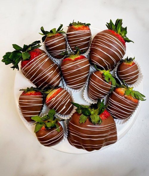 A plate of chocolate-covered strawberries drizzled with white chocolate, arranged neatly with green leaves.