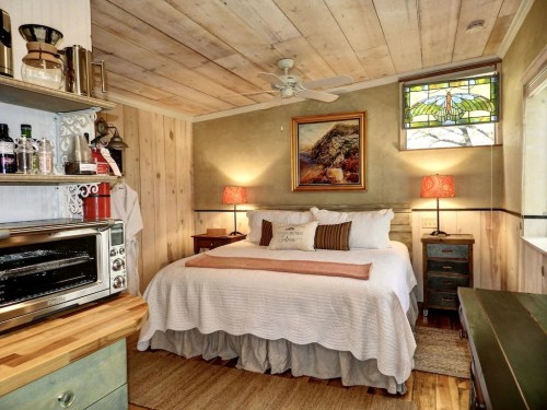 Cozy bedroom with a wooden ceiling, a queen bed, two lamps, and a stained glass window, featuring warm, inviting decor.