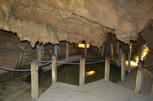 A dimly lit cave interior with wooden walkways and a small pool of water surrounded by rocky formations.