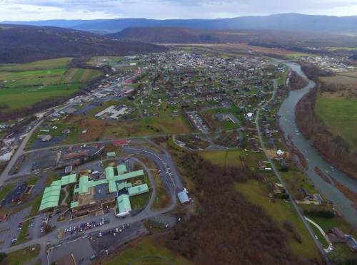 Aerial view of a small town with green fields, a river, and a mix of residential and commercial buildings.