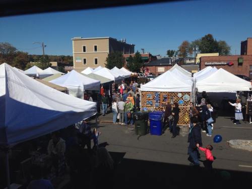 A bustling outdoor market with white tents, people browsing, and a clear blue sky overhead.