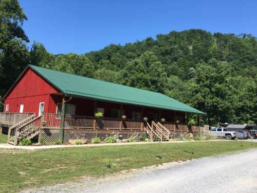 A red cabin with a green roof surrounded by trees and a gravel path on a sunny day.