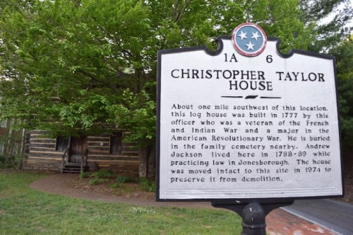 Historical marker for Christopher Taylor House, built in 1777, with a log house visible in the background.