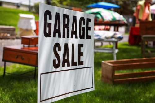 A sign reading "Garage Sale" in front of various items for sale on a sunny day.