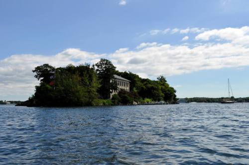 A view of a small island with a building surrounded by water under a blue sky with scattered clouds.