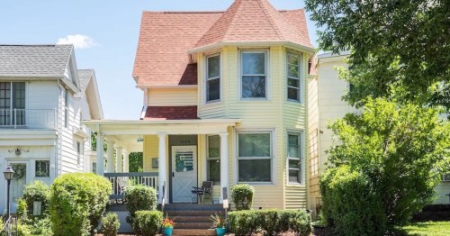 A charming yellow Victorian house with a steep roof, surrounded by greenery and a welcoming porch.