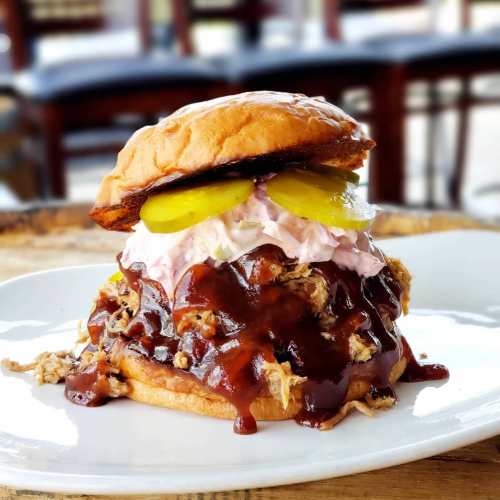 A close-up of a pulled pork sandwich topped with pickles and creamy sauce, served on a toasted bun.