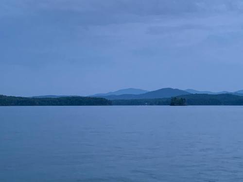 A serene lake scene at dusk, with distant mountains and a calm water surface reflecting the soft blue sky.