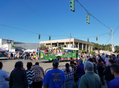 A colorful parade with a decorated float and a crowd of spectators under clear blue skies.