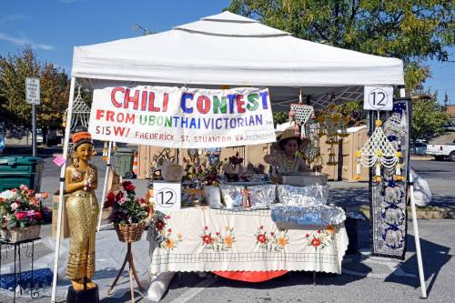 A vendor booth at a chili contest featuring a sign, decorations, and a person preparing food under a white tent.