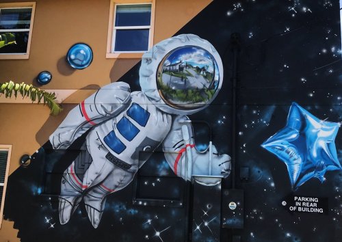 A colorful mural of an astronaut floating in space, with bubbles and a star, on a building's exterior wall.
