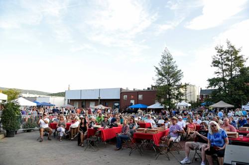 A large crowd enjoys an outdoor event with tables and tents under a clear sky.