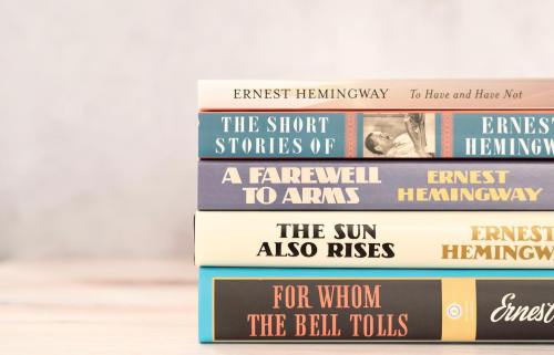 A stack of books by Ernest Hemingway, including titles like "A Farewell to Arms" and "For Whom the Bell Tolls."