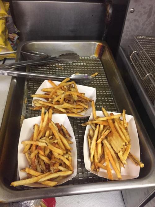 Three trays of golden-brown French fries on a metal rack in a kitchen setting.
