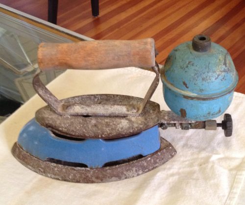 An antique blue and silver iron with a wooden handle and a steam reservoir, resting on a white cloth.