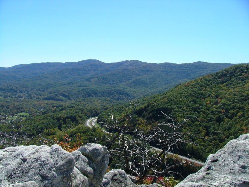 A panoramic view of rolling green mountains and a winding road under a clear blue sky.