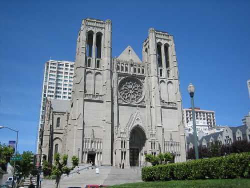 A large stone cathedral with twin towers and a rose window, set against a clear blue sky and urban backdrop.