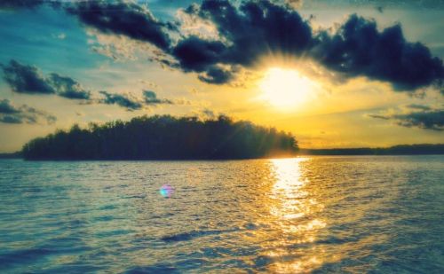 Sunset over a tranquil lake, with golden light reflecting on the water and clouds scattered in the sky.