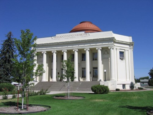 Historic courthouse with a domed roof, columns, and landscaped grounds under a clear blue sky.