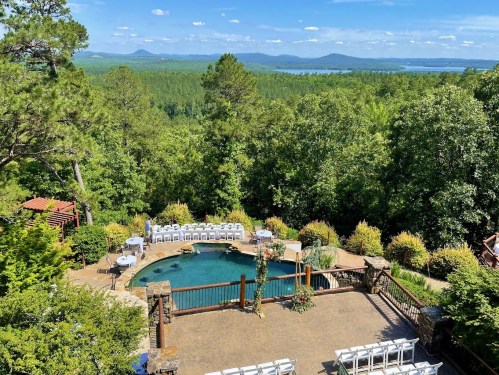 A scenic outdoor venue with a pool, surrounded by lush greenery and mountains in the background under a clear blue sky.
