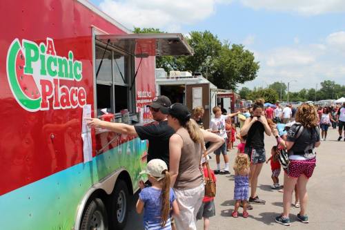 A food truck named "A Picnic Place" with a line of people waiting to order on a sunny day at an outdoor event.