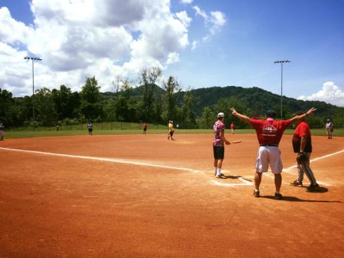 A sunny day at a softball field with players in action and mountains in the background.