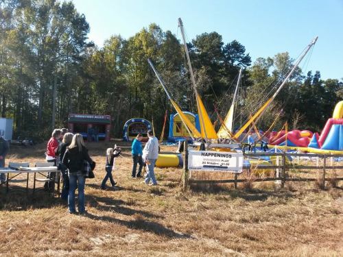 A lively outdoor fair with inflatable attractions, a bungee trampoline, and people enjoying the festivities.