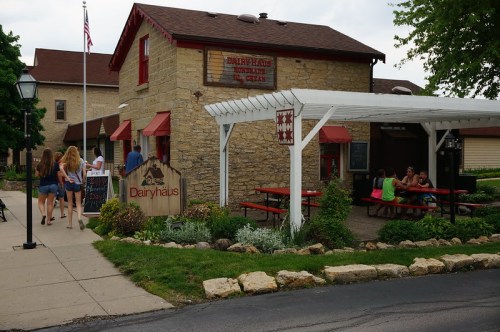 A charming stone building with a sign reading "Dairyhaus," featuring outdoor seating and people enjoying the space.