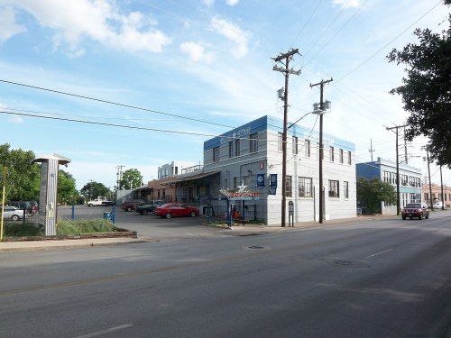 A blue and white building on a street with parked cars and power lines under a partly cloudy sky.