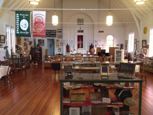 Interior of a museum with display cases, historical artifacts, and banners, featuring wooden floors and a welcoming atmosphere.