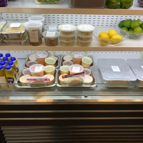 A refrigerated display with various food containers, sauces, and fresh produce like lemons and limes.