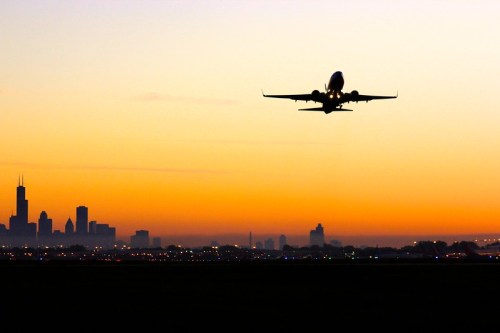 Silhouette of an airplane taking off against a vibrant sunset with a city skyline in the background.