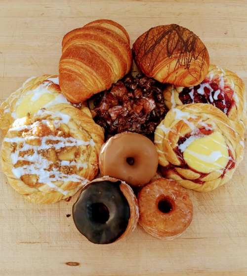 A variety of pastries arranged on a wooden surface, including croissants, donuts, and fruit-filled danishes.