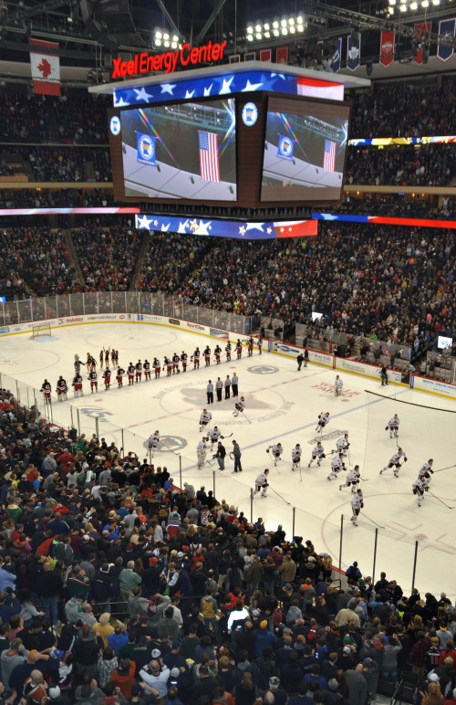 A packed arena at the Xcel Energy Center during a hockey game, with players on the ice and fans in the stands.