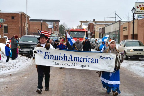A winter parade in Hancock, Michigan, featuring participants carrying a banner for the Finnish American Reporter.