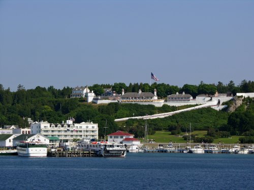 A scenic view of a harbor with boats, a hotel, and a hillside featuring a flag and historic buildings.