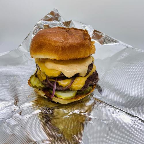 A delicious burger with two patties, melted cheese, pickles, and sauce, served on a toasted bun, wrapped in foil.