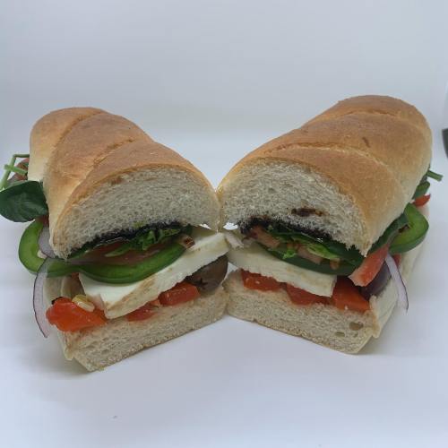 A freshly cut sandwich with layers of vegetables, cheese, and sauce, served on a toasted baguette.