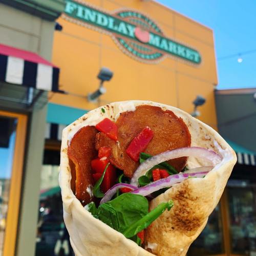 A delicious wrap filled with vegetables and meat, with a market backdrop featuring a colorful sign.